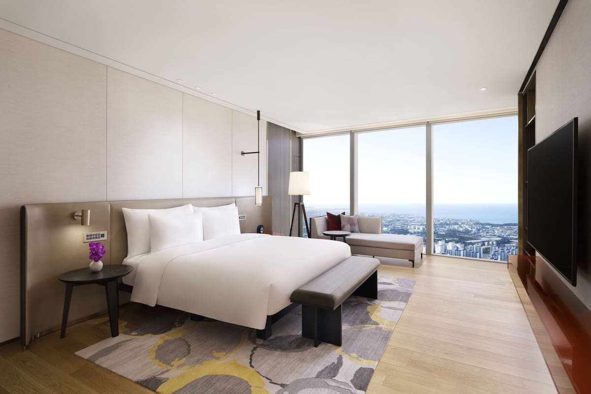 Ein modernes Hotelzimmer mit einem großen Bett, einer Sitzecke, einem Fernseher und Blick auf die Stadt.