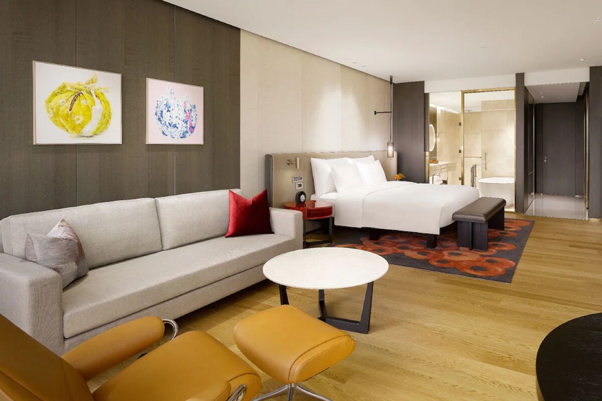 A modern hotel room with a sofa, a bed, a round coffee table, and a TV.