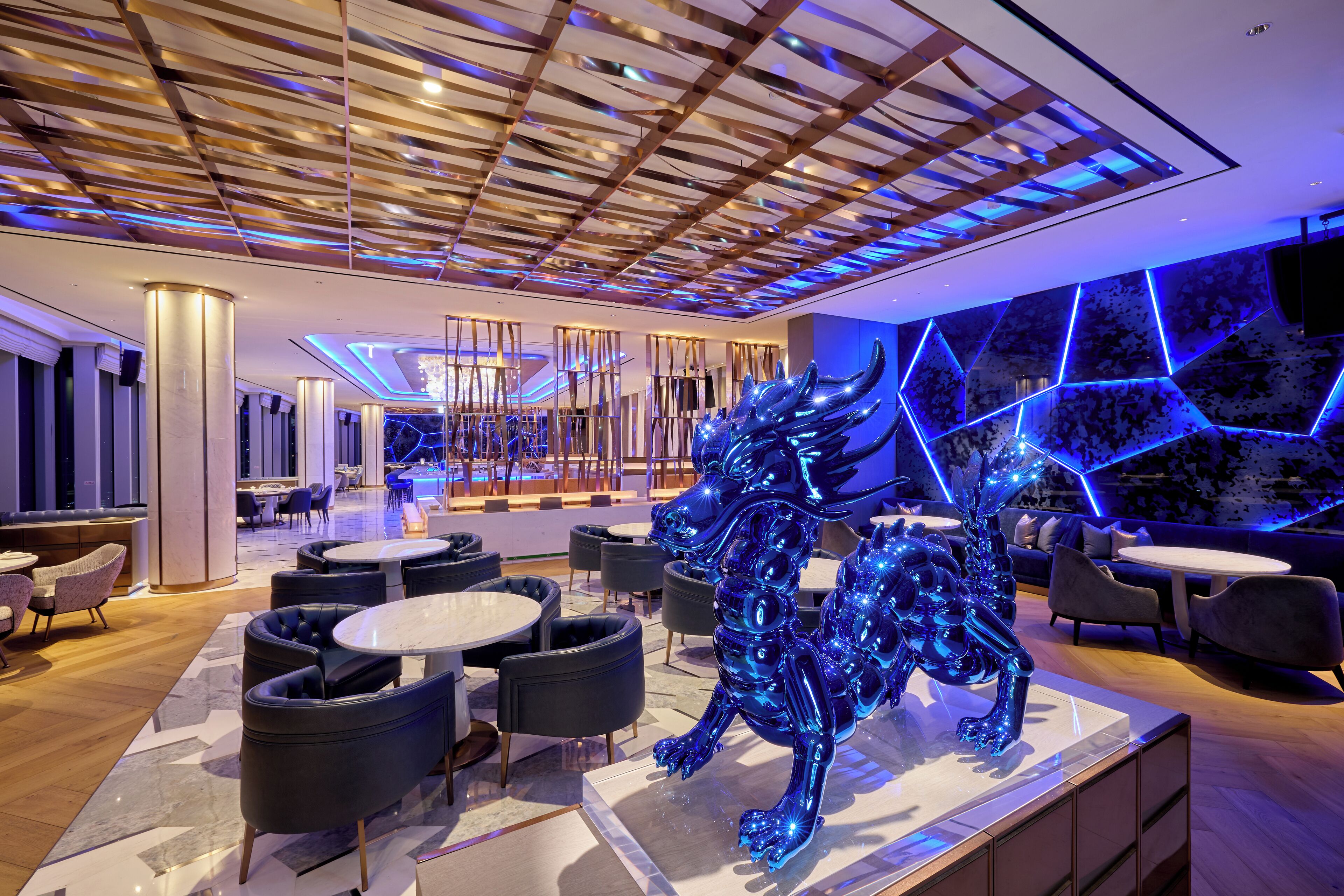 A modern hotel lobby with a central seating area, a large metallic sculpture, and a geometric-patterned wall.
