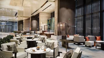 A spacious lobby with multiple seating areas, including sofas and round tables, and a large glass entrance.
