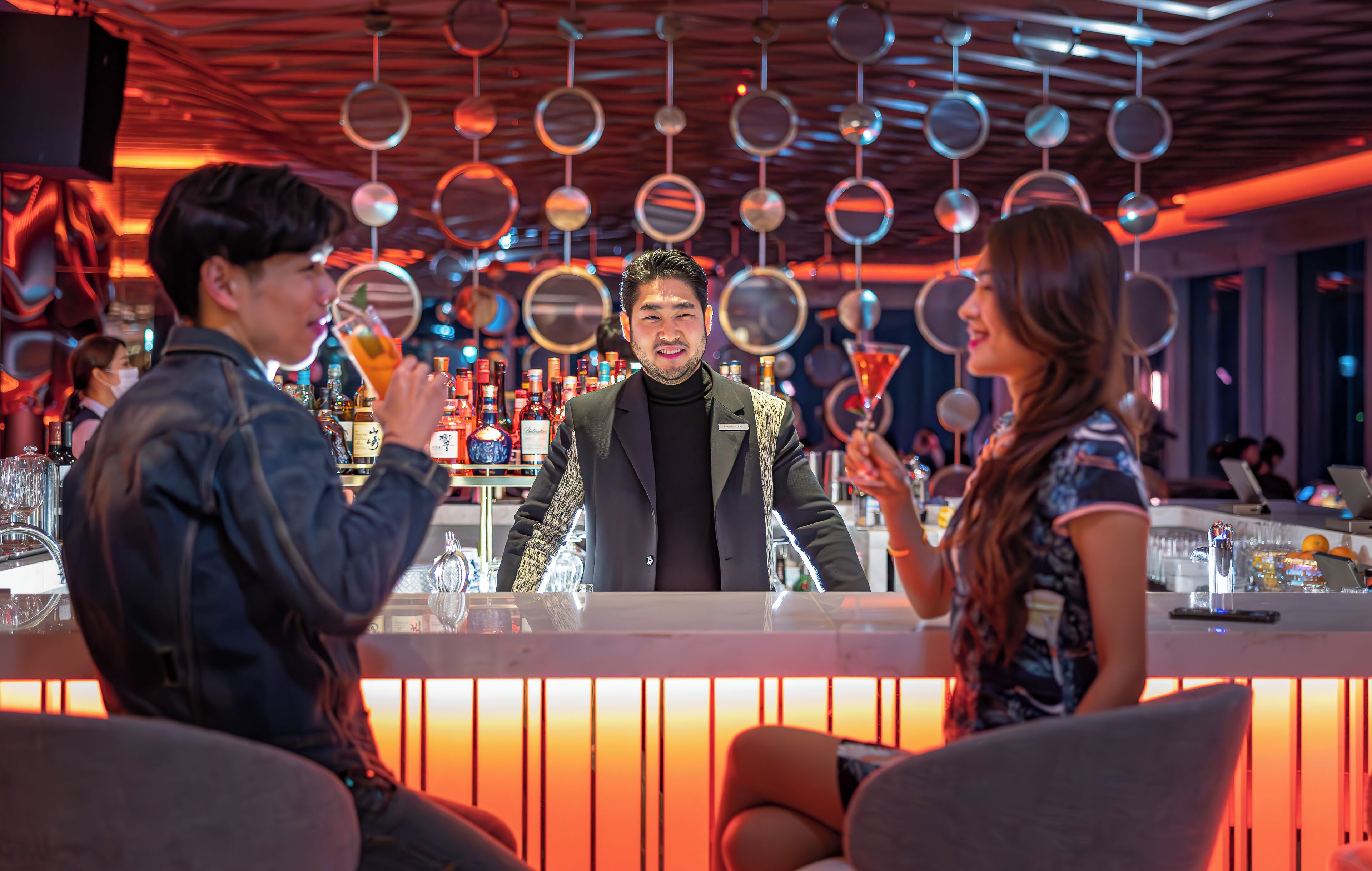 A bar area with a modern design, featuring hanging mirrors and a variety of bottles.