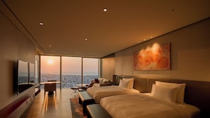 A modern hotel room with a large bed, a desk, and a chair. There is a large window with a view of the city. - Grand Hyatt Jeju (Jeju City)