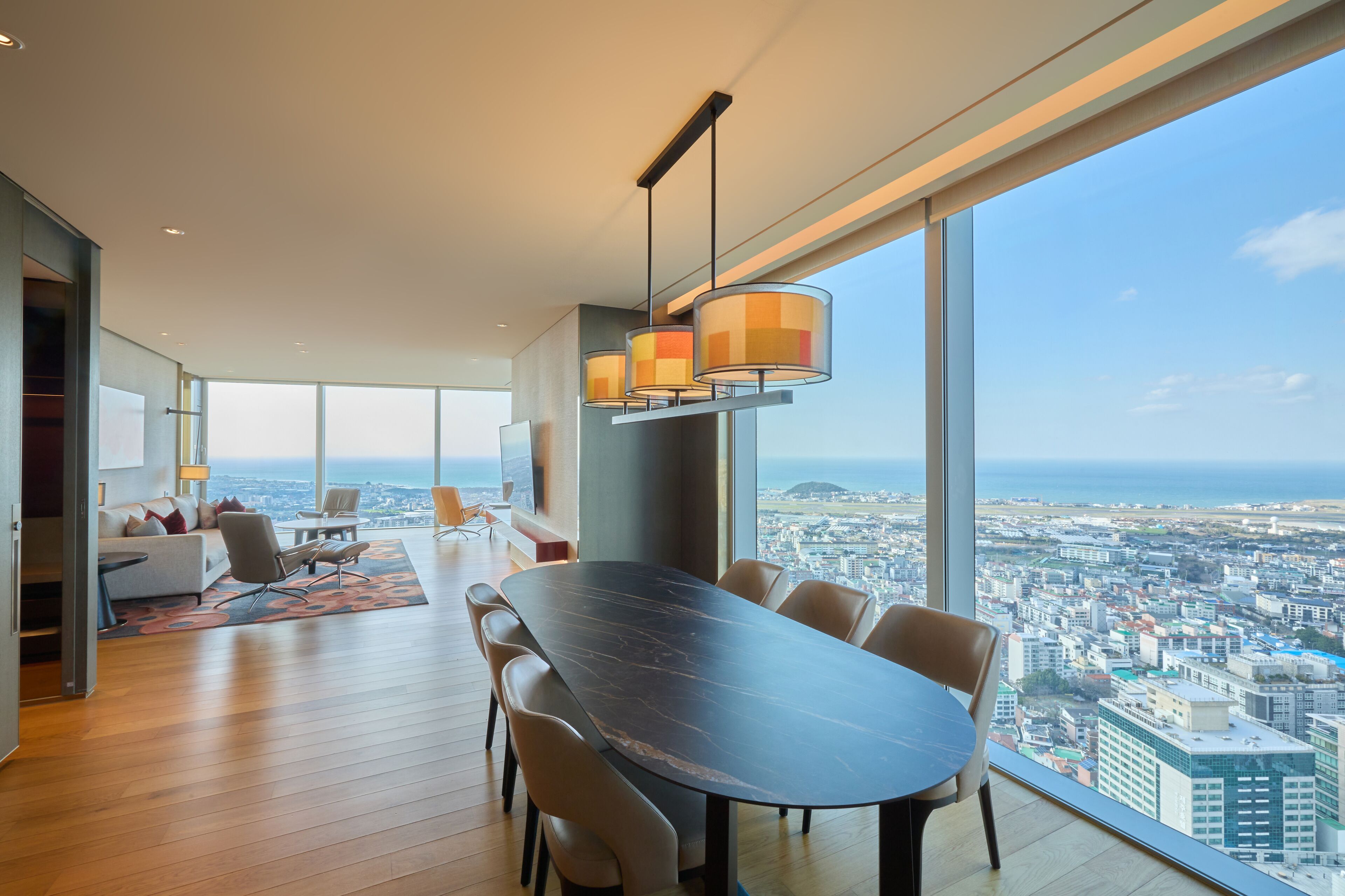 A spacious living area with a large dining table, comfortable seating, and a city view through large windows.
