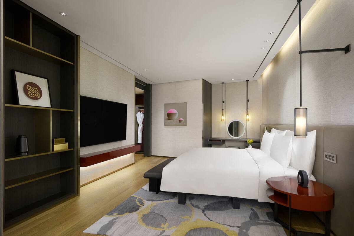 Ein modernes Hotelzimmer mit einem großen Bett, einem Fernseher, einem Nachttisch, einem Spiegel und einem Kleiderschrank.
