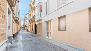 Une rue étroite, bordée de bâtiments des deux côtés, dont l’un affiche une enseigne sur laquelle on peut lire : « À VENDRE 936 800 700 ».