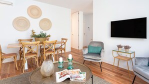 A modern living room with a dining area, a grey sofa, a TV mounted on the wall, and a small side table with plants. - Genteel Home San Antonio Terrace II (Cadiz)