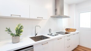 A modern kitchen with white cabinetry, a stainless steel sink, a built-in range hood, and a window providing natural light. - Genteel Home San Antonio Terrace II (Cadiz)