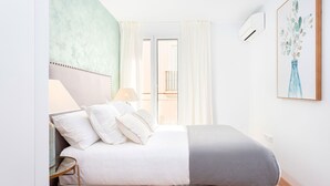 A bedroom with a bed, pillows, a bedside table, a lamp, a window with curtains, and a wall-mounted air conditioner. - Genteel Home San Antonio Terrace II (Cadiz)