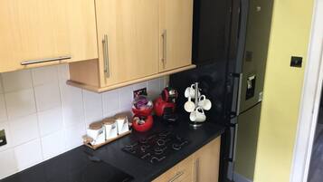 A kitchen with wooden cabinets, a black countertop, a red coffee machine, and a black refrigerator.