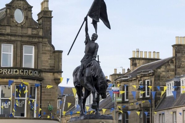 A statue of a figure on horseback with a raised flag, set against a backdrop of historic buildings and a clear sky. - Lovely 2- Bed Apartment in Hawick (Hawick)