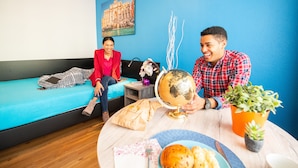 Una habitación con pared azul, una cama, una mesa redonda con un globo terráqueo, una planta y un plato de comida.