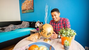 Una persona sentada a una mesa redonda con un globo terráqueo, una planta y un plato con panecillos.