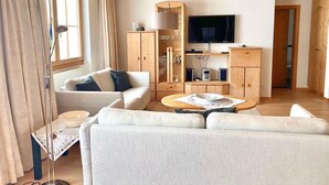 En moderne stue med sofa, sofabord, fjernsyn, træskabe og en gulvlampe.