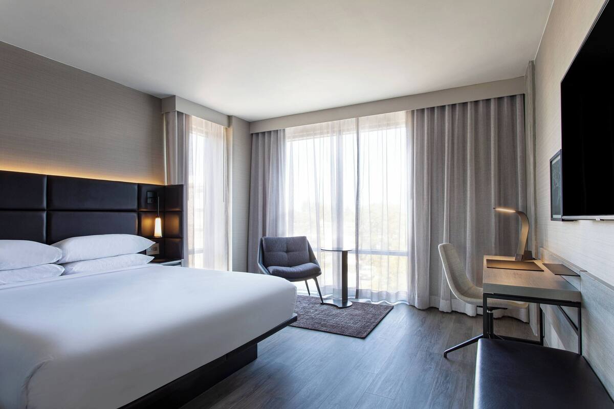 A modern hotel room with a large bed, a desk, a chair, and a TV.
