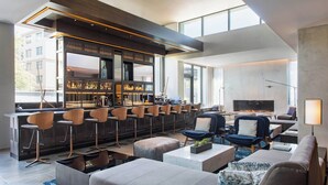 A modern bar area with high stools, a seating area with sofas and armchairs, and a large TV screen.