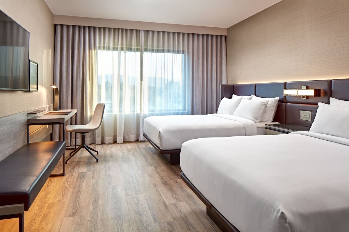 A hotel room with two beds, a desk, a chair, and a TV.