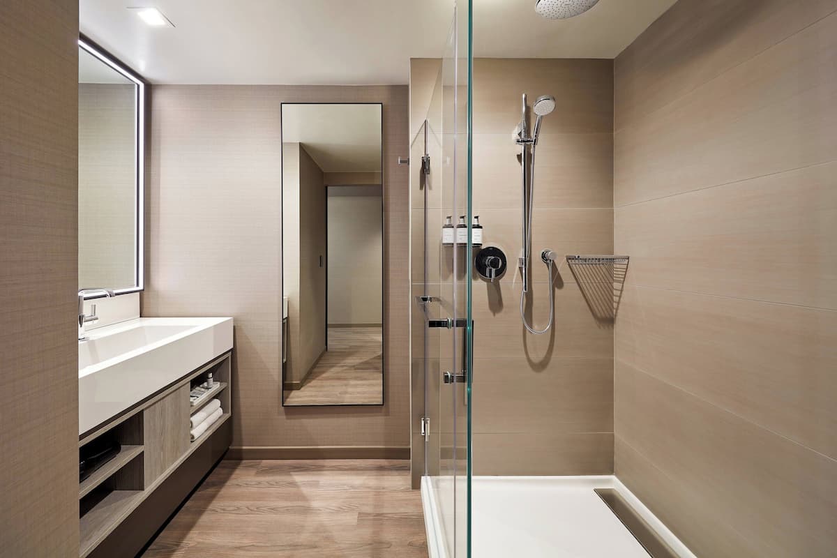 Ein modernes Badezimmer mit einer gläsernen Dusche, einem großen Spiegel und einem hölzernen Waschtisch.