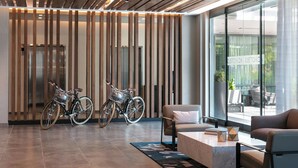 A modern lobby with two bicycles, a sofa, a coffee table, and a large window with a view of outdoor seating.