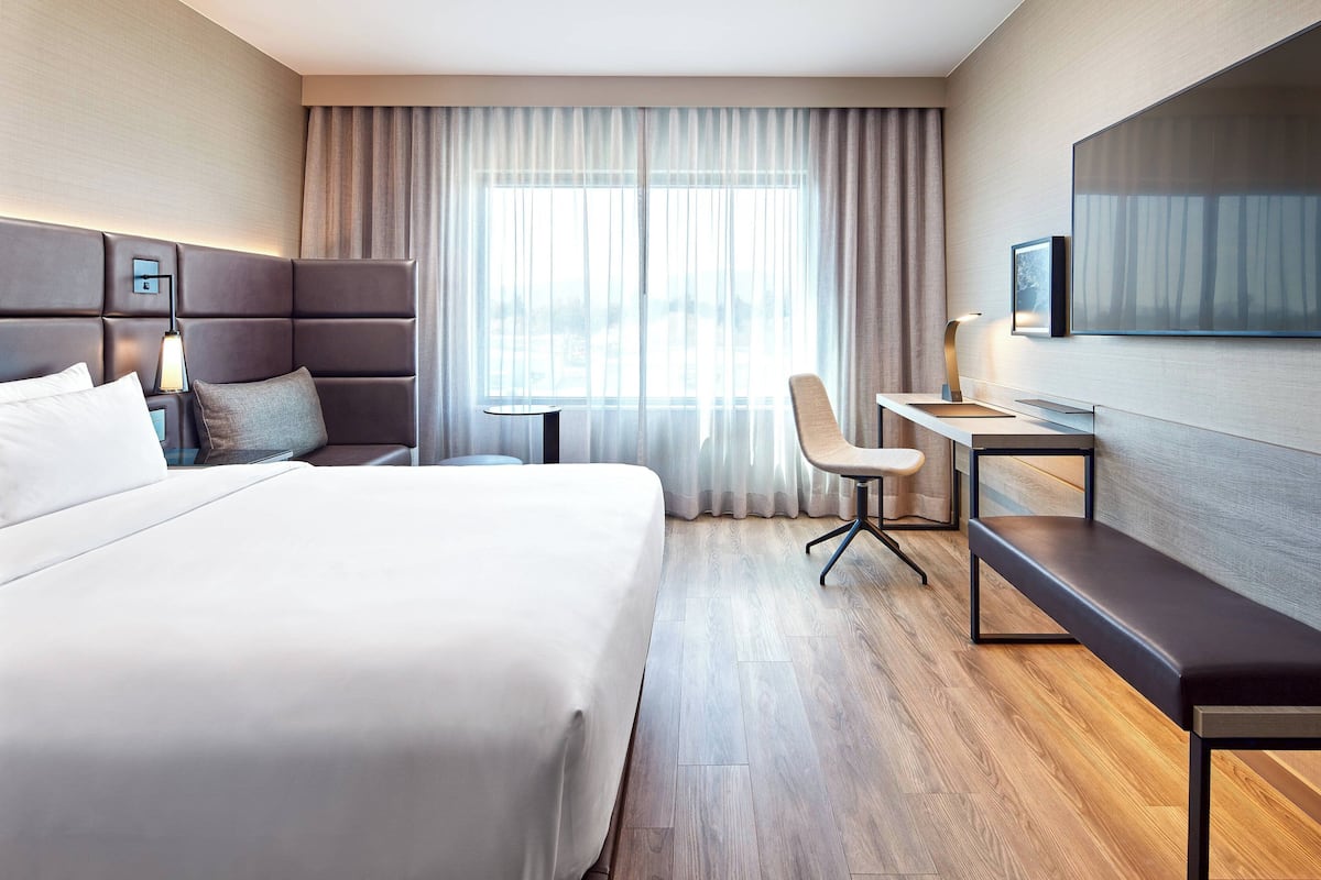A hotel room with a large bed, a desk, a chair, a TV, and a window with curtains.