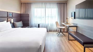 Une chambre d’hôtel avec un grand lit, un bureau, une chaise, une télévision et une fenêtre avec des rideaux.