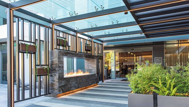 A modern hotel lobby with a glass ceiling, a fireplace, and a seating area with plants.