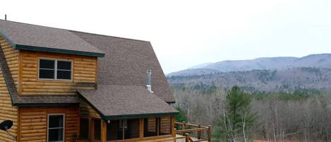 A log cabin with a balcony and a view of a forested mountain range.
