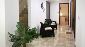 Een gang met een potplant, twee zwarte stoelen, een trap en een deur naar een andere kamer.