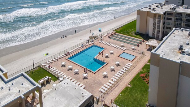 Zona de piscina en la azotea con dos piscinas, tumbonas y vistas a la playa y el océano.