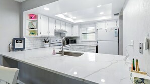 Una cocina moderna con armarios blancos, encimera de mármol y horno empotrado.