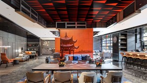 Un hall d’entrée spacieux avec un espace salon central, un bar et un grand écran numérique affichant une image d’un bâtiment traditionnel d’Asie.