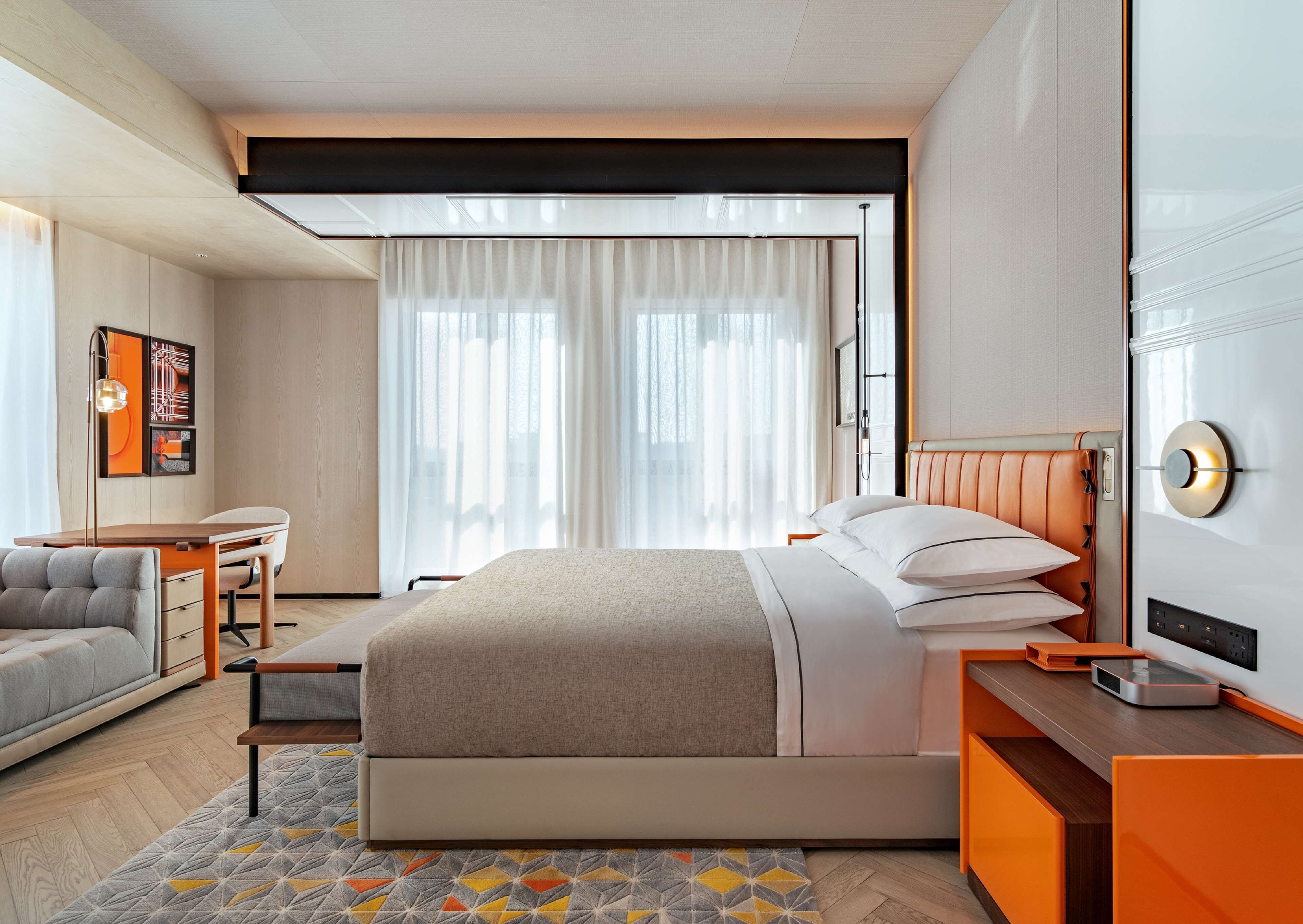 A modern hotel room with a large bed, a desk, a chair, and a TV.