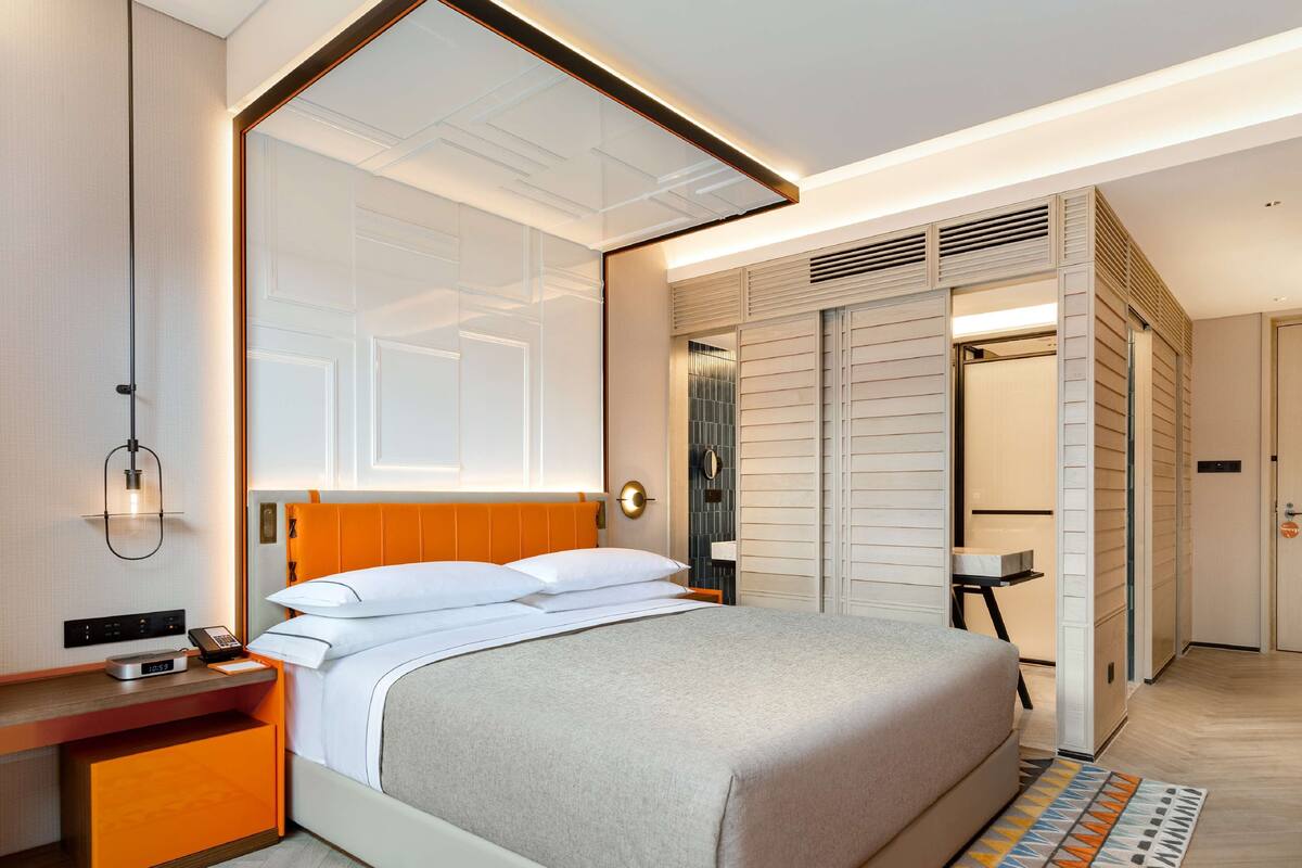Una habitación de hotel moderna con una cama grande, una mesita de noche con teléfono y despertador, un armario con puertas correderas y una alfombra estampada.