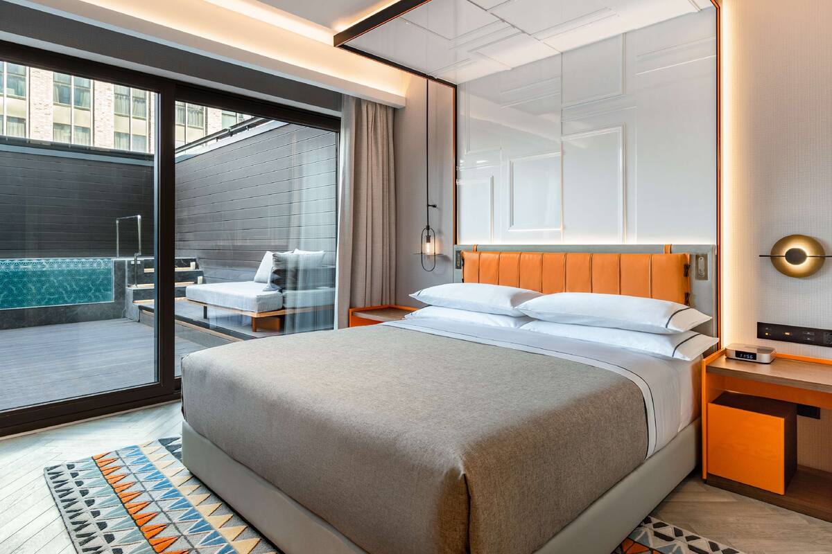 Habitación de hotel moderna con una cama grande, un pequeño rincón de descanso con vistas al exterior y un balcón privado.