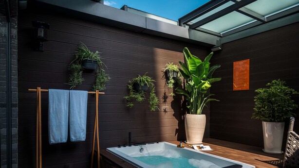 Un espace de détente extérieur moderne, doté d’un jacuzzi, d’une terrasse en bois et de divers pots de plantes.