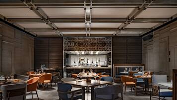 A spacious dining area with multiple tables and chairs, a central bar area, and a modern ceiling design.