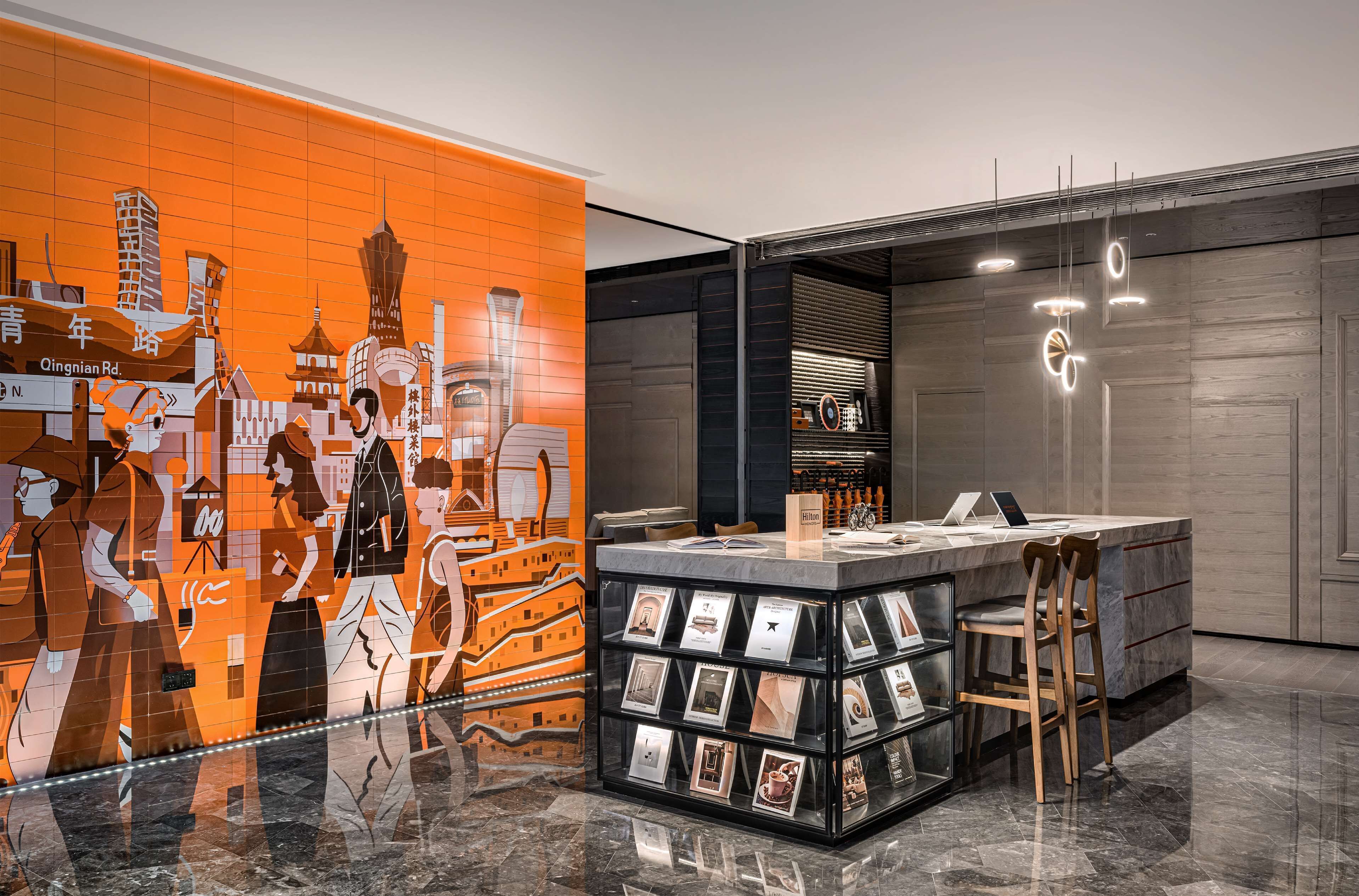 En moderne hotellobby med et bybillede som muralmaleri, en receptionsdisk og en udstilling af indrammede billeder.