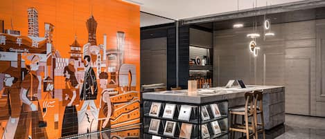 A modern hotel lobby with a cityscape mural, a reception desk, and a display of framed photos.