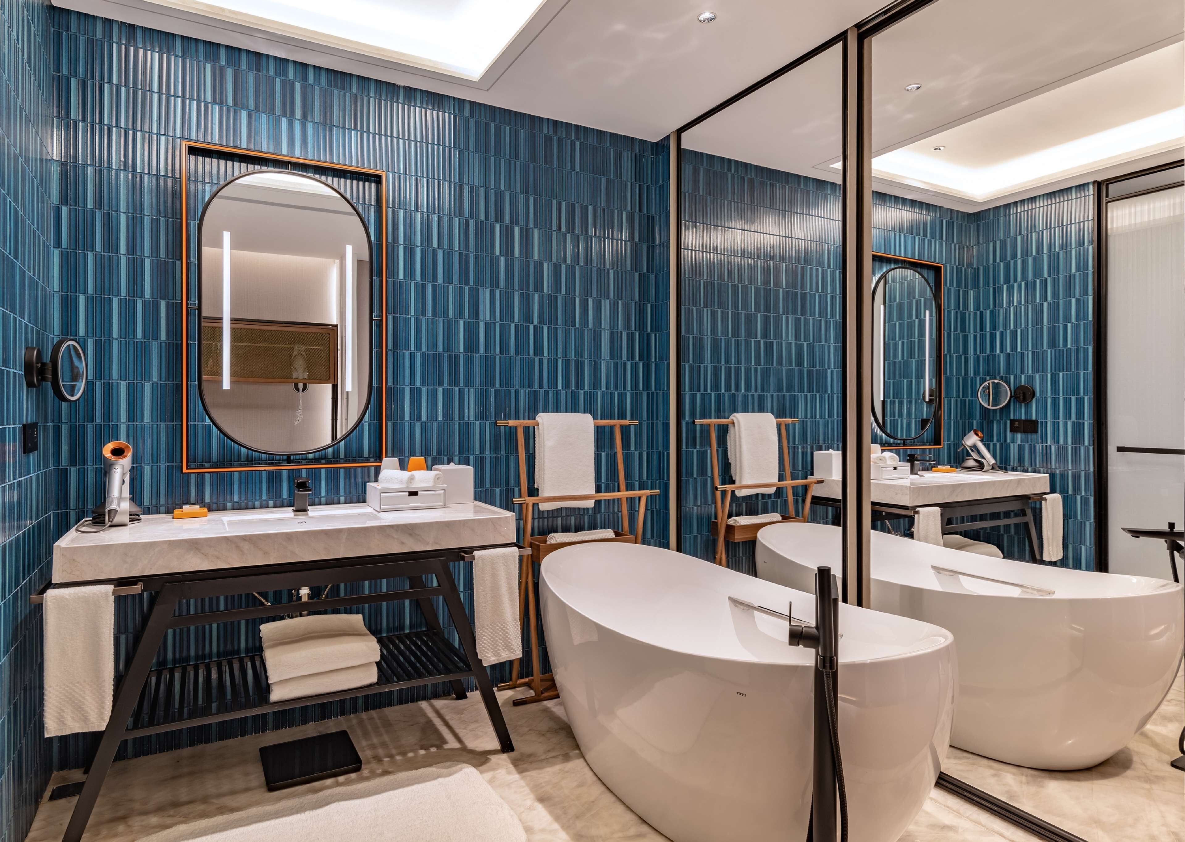 Ein modernes Badezimmer mit blauen Fliesen, einem großen Spiegel, einem Waschtisch und zwei separaten Badewannen.