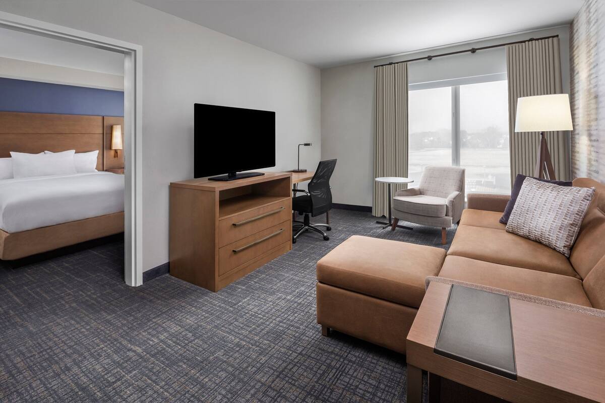 A hotel room with a bed, a desk with a TV, a sofa, and a chair.