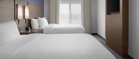 A hotel room with two beds, a TV mounted on the wall, and a large window with curtains.