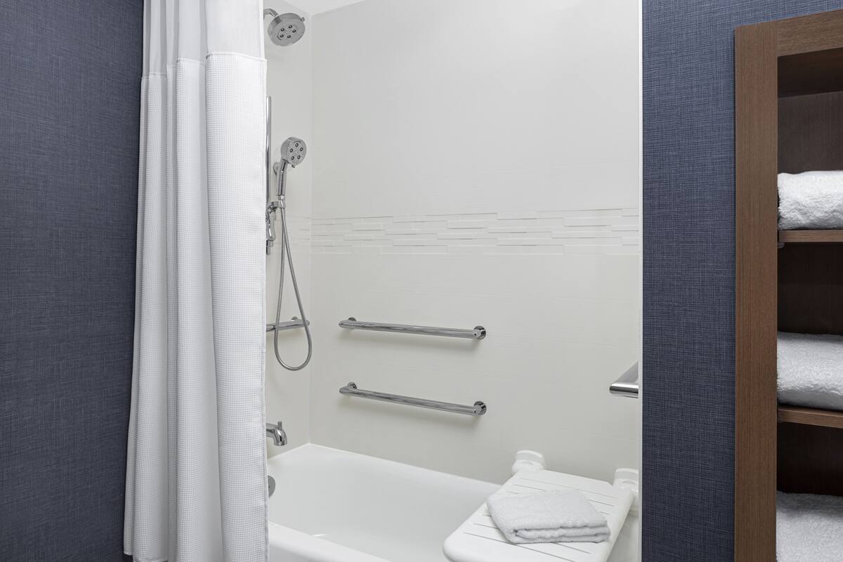 A modern bathroom with a shower, grab bars, and a white bathtub.