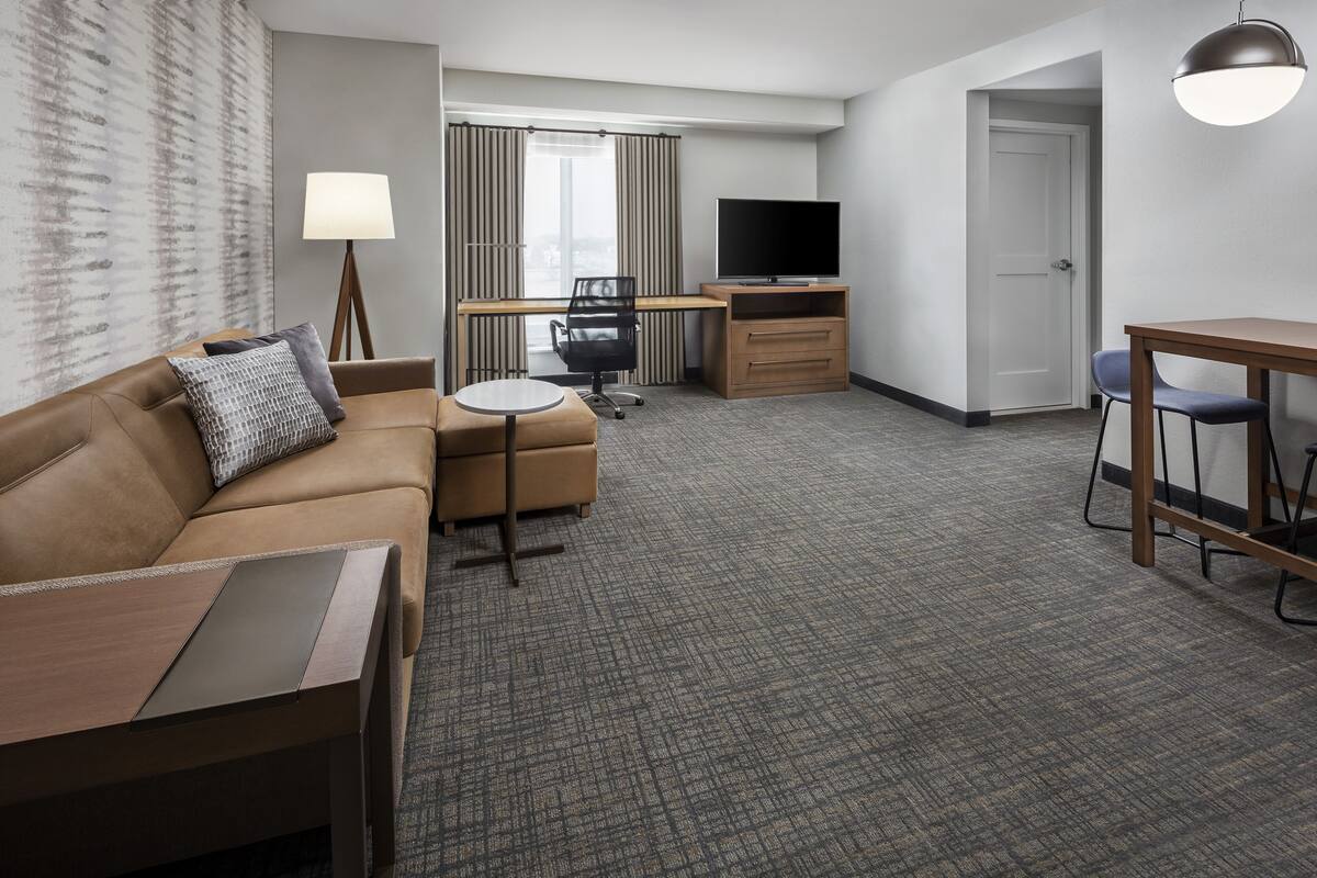 A hotel room with a sofa, a small table, a desk with a computer, a TV, and a chair.