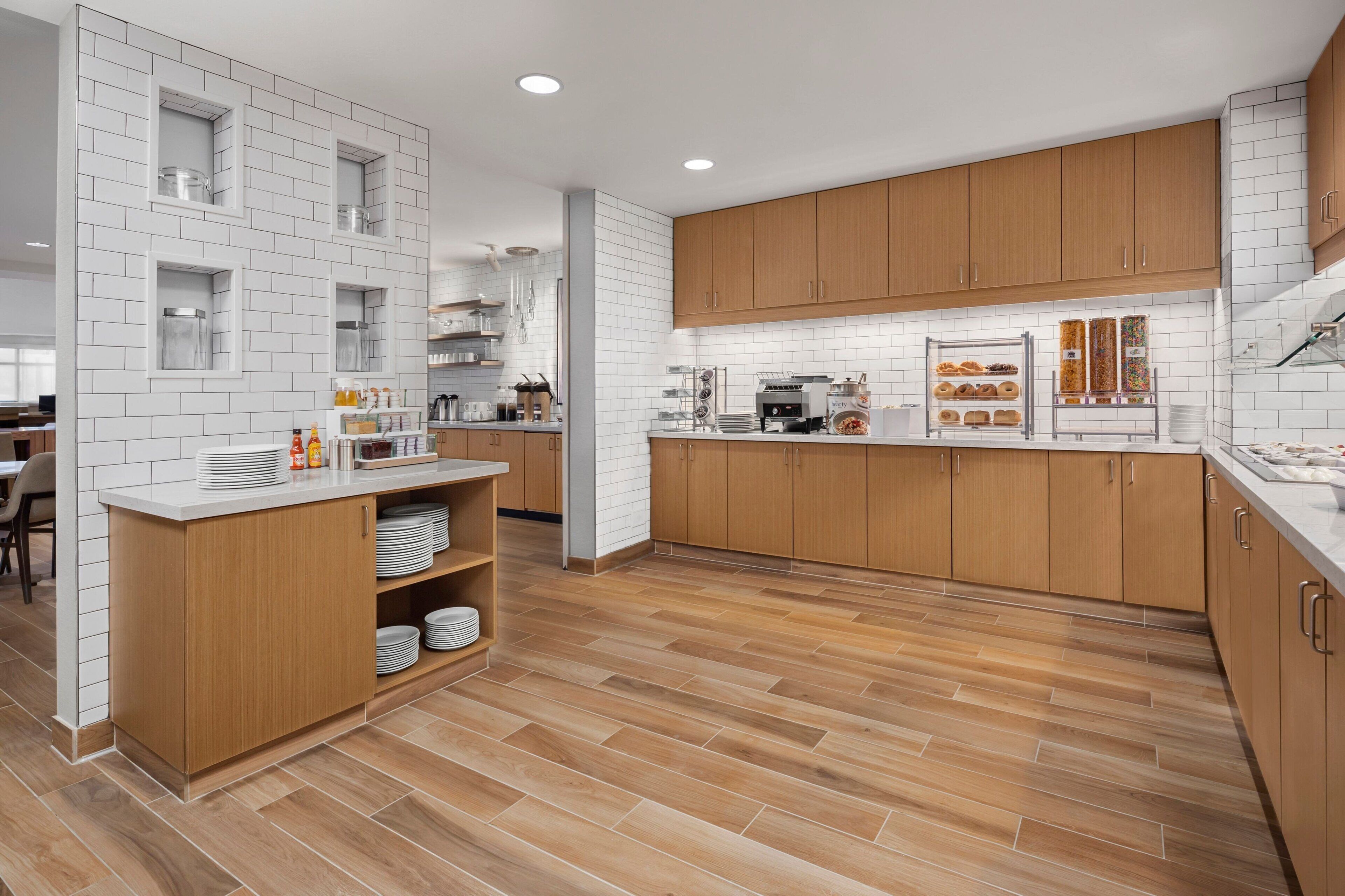 A modern kitchen with wooden cabinets, white tiled backsplash, and a wooden floor.