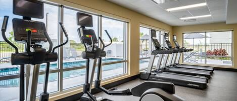 A gym with multiple treadmills and elliptical machines, large windows with a view of a swimming pool and outdoor area.