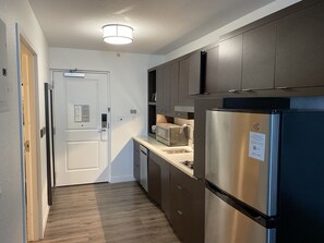Cocina compacta con armarios oscuros, refrigerador de acero inoxidable, microondas y lavavajillas.