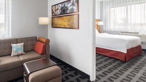 Hotellihuoneessa on sohva, sänky, pieni pöytä ja kaksi kehystettyä kuvaa seinällä.