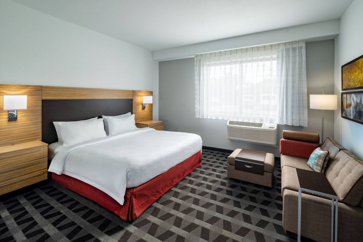 A hotel room with a bed, bedside tables, a sofa, a small table, and a window with curtains.