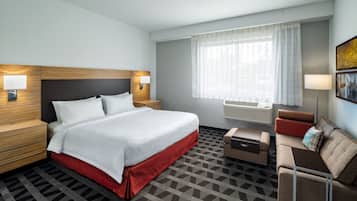 Quarto de hotel com cama, mesas de cabeceira, sofá, uma pequena mesa e janela com cortinas.