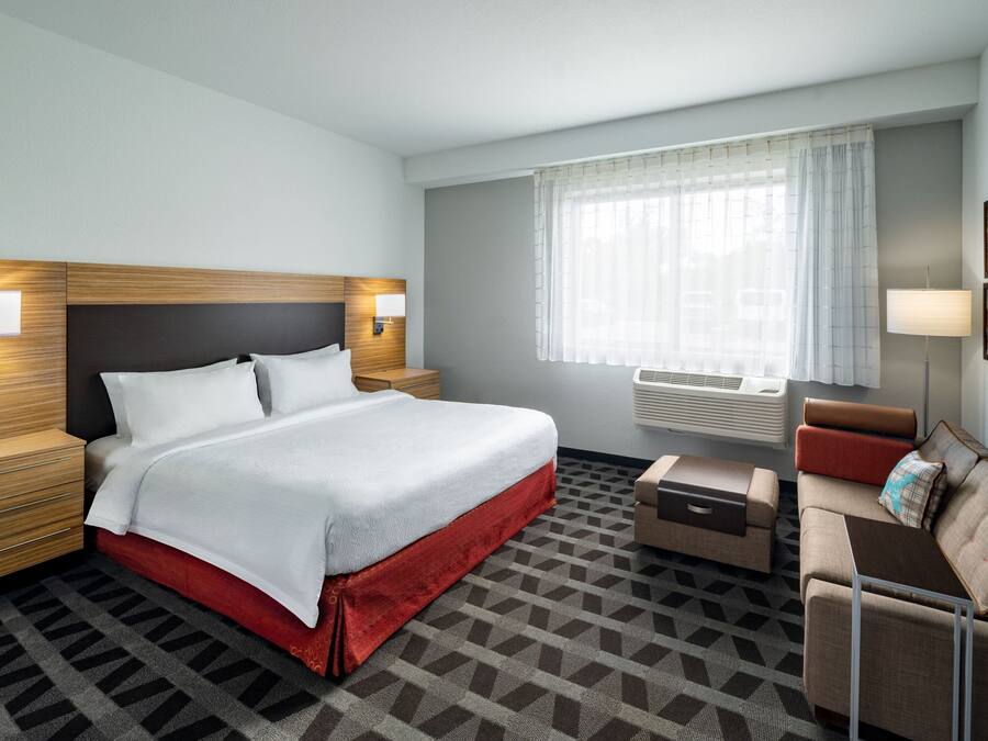 Ein Hotelzimmer mit Bett, Nachttischen, einer Couch, einem kleinen Tisch und einem Fenster mit Vorhängen.