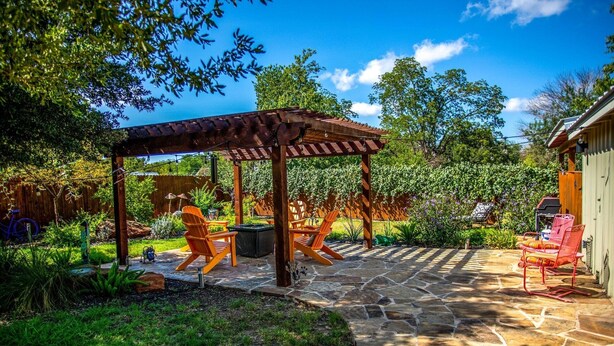 A covered patio area with stone flooring, wooden pergola, and outdoor seating.